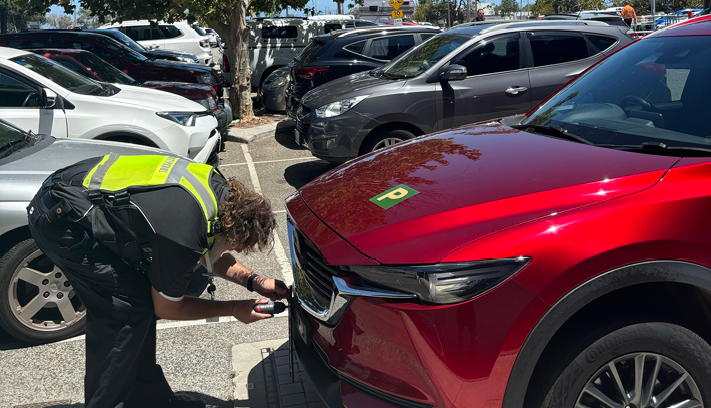 Image of a community patrol officer fixing anti theft screws to number plate on a red car in a car park